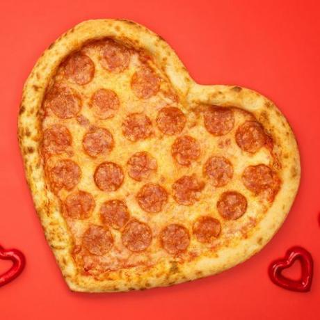 Peperoni pizza a forma di cuore per San Valentino su sfondo di carta rossa