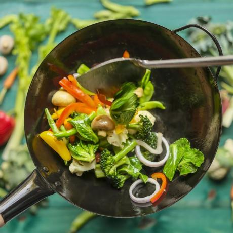 mescolare e soffriggere una varietà di verdure fresche e colorate in un wok caldo e fumante con verdure su uno sfondo di tavolo di legno color turchese sotto il wok